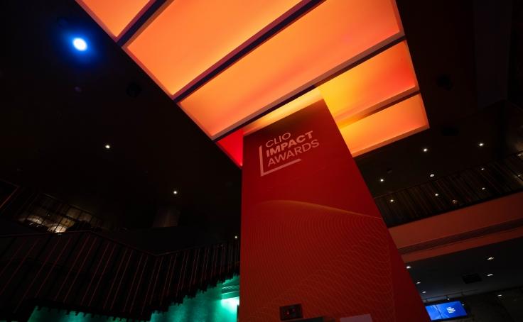 Un espace intérieur illuminé en rouge et orange présentant un panneau pour les Clio Impact Awards.